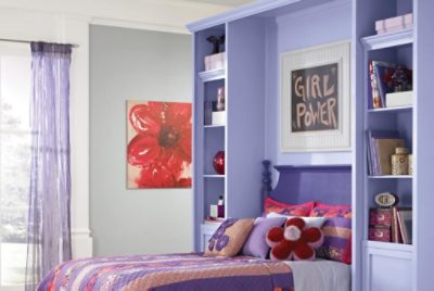 A child's bedroom with purple built-in shelving on the wall the headboard rests against.