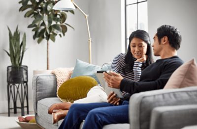 Two people sitting on a couch looking at a tablet together.