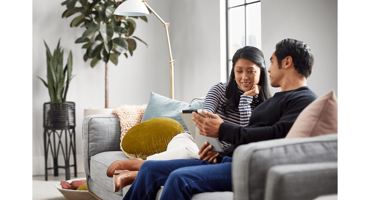 Two people sitting on a couch looking at a tablet together.