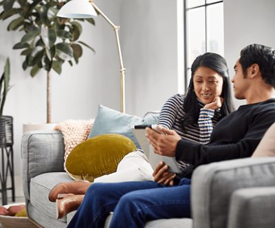Two people sitting on a couch looking at a tablet together.