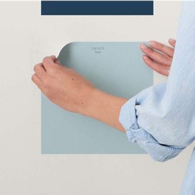 A person applying a Peel and Stick color sample to a wall.