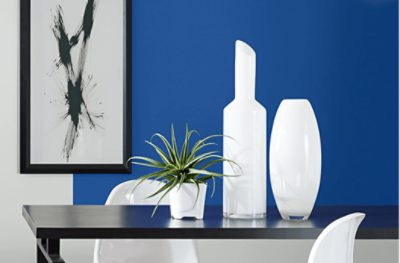 Wall painted in SW 6967 Frank Blue with a simple black frame, black table with white chairs and decor.
