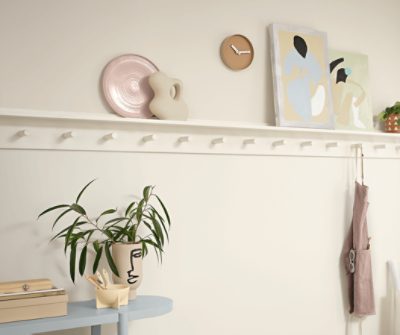 Up close of a narrow shelf holding art pieces on a wall painted Alabaster SW 7008. with many pegs and an apron hanging from one.