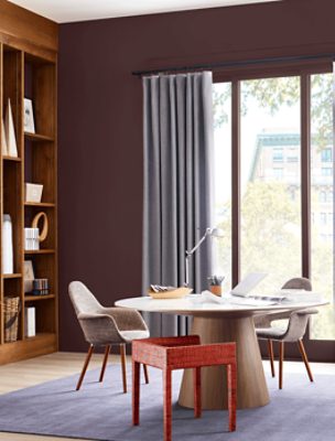 A table with a laptop and light in front of sliding door with walls painted Carnelian SW 7580.