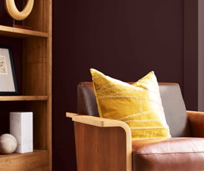 A leather armchair next to a wooden bookshelf against a wall painted Carnelian SW 7580.