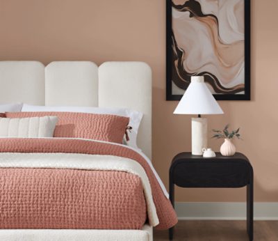Bedroom with coral bedspread, white headboard, bedside table with lamp.