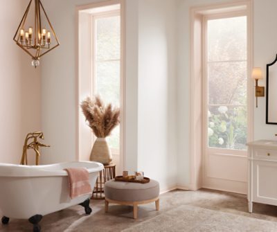 A bathroom with a freestanding tub, stool, chandelier and large windows.