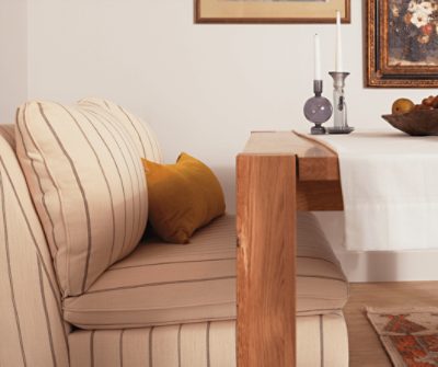 Walls painted Eider White SW 7014 next to a sofa being used as seating at a dining table.