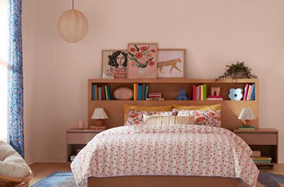Bedroom painted in SW 6610 Koral Kicks, with wooden bookshelf behind the bed with a printed bedspread.