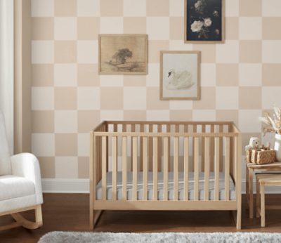 Nursery painted in a checkered pattern with Sand Dollar SW 6099, paintings, rocking chair, and crib.