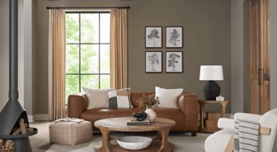 Living room painted in SW 9172 Studio Clay with brown leather couch, some tree prints on the wall, large window and minimal decor.