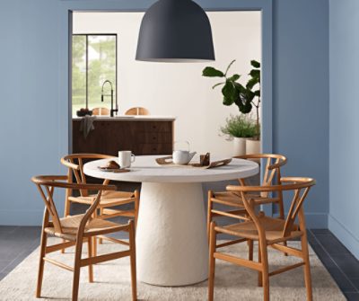 A round off-white table with a large black pendant light overhead in a dining area painted Aleutian SW 6241.