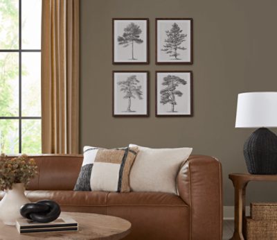 Living room painted in SW 9172 Studio Clay with brown leather couch, some tree prints on the wall and minimal decor.