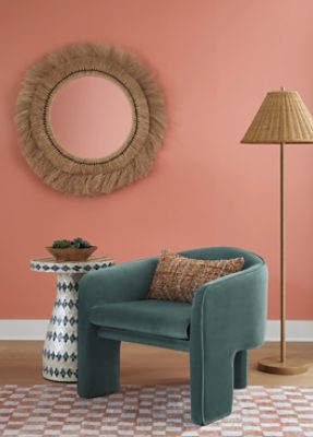 Walls painted in SW 6332 Coral Island, with a decorative mirror, green chair, side table, and standing lamp.