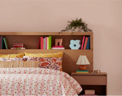 Bedroom painted in SW 6610 Koral Kicks, with wooden bookshelf behind the bed with a printed bedspread.