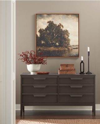 Walls painted in SW 7012 Creamy with a dresser with decor and candlesticks on top with a painting above it.