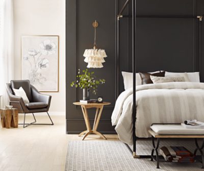 A canopy bed with black rails next to a small nightstand and chair.