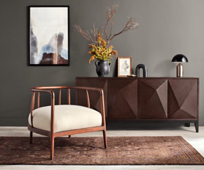 A chair with large white cushion on a rug next to a dark stained dresser.