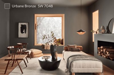 A bedroom with a small bed, modern black table with art, 2 wooden chairs and a fireplace.