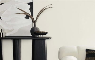 A side table and upholstered chair in front of a wall painted Heron Plume.