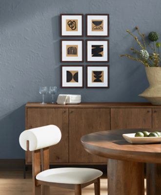 Round wooden table with a chair with white cushions, wooden credenza behind it with some artwork hung on a wall painted in SW 6249 Storm Cloud.