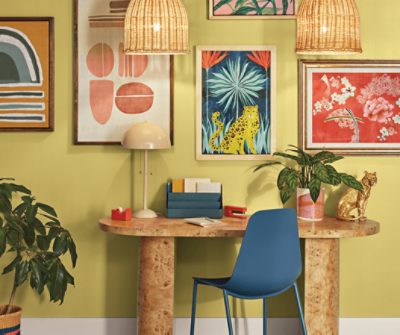 An oval desk against a wall painted in SW 0073 Chartreuse with a collage of prints.