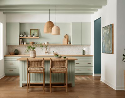 Kitchen cabinets painted in SW 6176 Liveable Green, wicker bar stools, overhead lamps, and light decor.