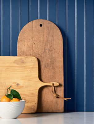 A bowl of oranges and two cutting boards against a backsplash painted in SW 6524 Commodore.