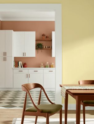 Side of kitchen table and chairs, wall painted in SW 1667 Icy Lemonade, with white cabinets and checkered floor behind it.