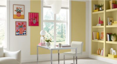 Shelves painted in SW 1667 Icy Lemonade, with bright decor and books, white desk and chair in front of them, windows and floral paintings on the other wall.