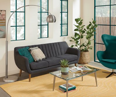 Living space with a couch, green chair, small glass table and large silver arched floor lamp.