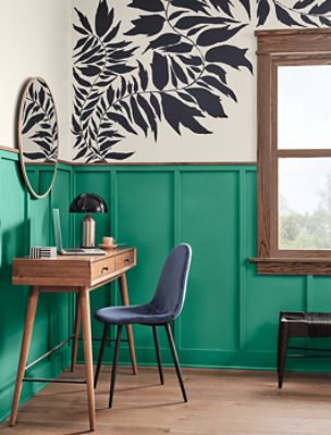 A small table and blue velvet chair in front of a mirror in a bedroom with board and batten painted Alexandrite SW 0060.