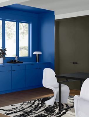 Wall with windows painted in SW 6967 Frank Blue, has cabinets underneath, gray double doors to the right of that, black table with white chairs sitting on an a rug.