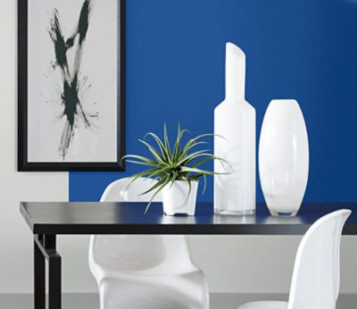 Wall painted in SW 6967 Frank Blue with a simple black frame, black table with white chairs and decor.