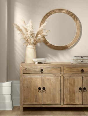 Wall painted in SW 9173 Shiitake, round mirror hung, wooden dresser with minimal decor on top.