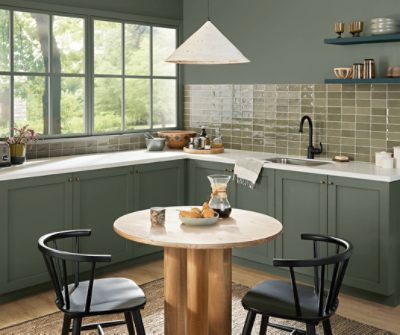 A kitchen with lower cabinets and walls above a warm tan glass backsplash painted Rosemary SW 6187.