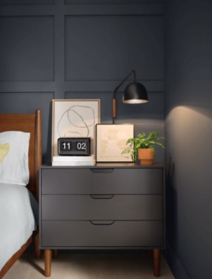 A dark mid-century modern night stand against a wall painted in SW 7076 Cyberspace.