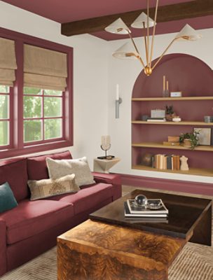 A living room with a maroon couch, wood carved coffee table and built in arched shelves.