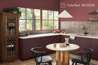 A kitchen with a circular table and 2 black chairs, overhead light and maroon colored walls.