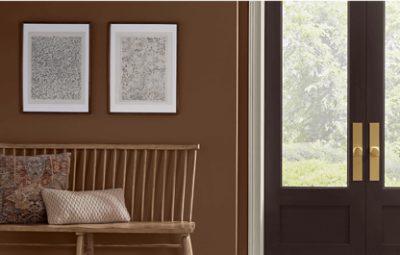 Entryway double doors with windows, to the left walls painted in SW 6089 Grounded with two prints hanging and a wooden bench with pillows.