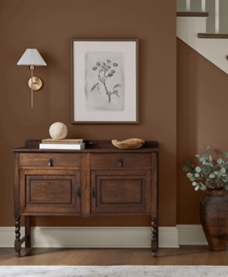 Walls painted in SW 6089 Grounded with wooden dresser with minimal decor on it, print hanging above it by a neutral staircase.