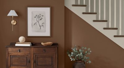 Walls painted in SW 6089 Grounded with wooden dresser with minimal decor on it, print hanging above it by a neutral staircase.