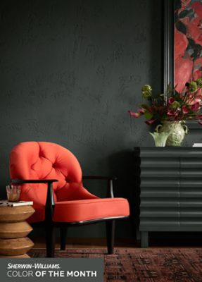 Sitting area with a bright coral chair, small wooden table and dresser, with walls painted in SW 7062 Rock Bottom.