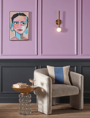 A modern chair and table in front of a two-toned wall with Novel Lilac SW 6836 above a dark gray.