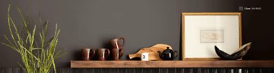 Wall painted Sherwin-Williams Clove SW9605 with dark brown mugs, a small black teapot, and a picture of a hand in a gold frame sitting on a wooden shelf.