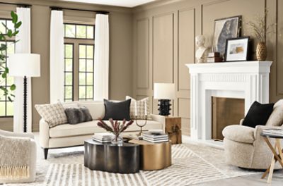 A large, bright living room with walls painted in SW 6150 Universal Khaki, large white fireplace, and beige colored furniture.