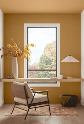 Small room painted Sherwin-Williams Bosc Pear SW6390 including a large window with a white painted frame and a light wooden desk with dark wooden flooring.