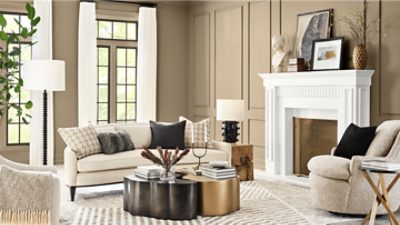 A large, bright living room with walls painted in SW 6150 Universal Khaki, large white fireplace, and beige colored furniture.
