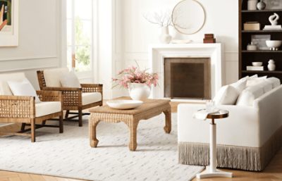 A bright living room with white walls with two wicker chairs across from a cream colored sofa.