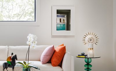 A modern sitting room in designer Seth Van Den Bergh’s studio with white furniture and colorful accents, including books, a sculpture, and an orchid on a glass table, painted Westhighland White by Sherwin-Williams.